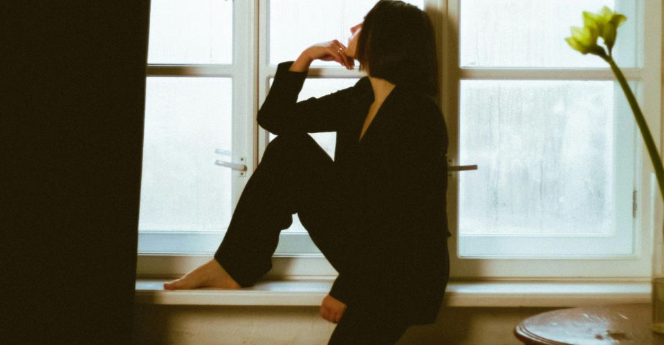 Vrouw die peinzend voor het raam staat — stoppen met een affaire voelt emotioneel zwaar