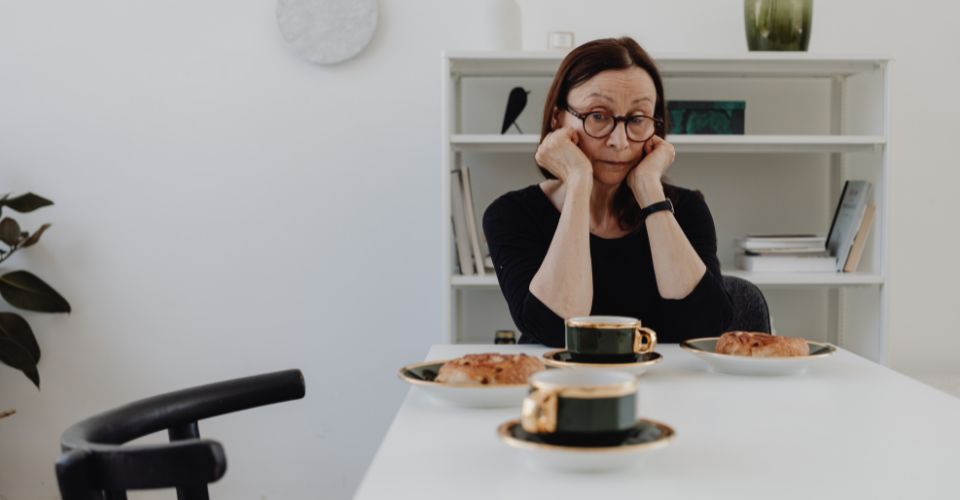 Vrouw zit alleen aan keukentafel, verdiepit in gedachten na ontdekking van emotioneel vreemdgaan van haar partner